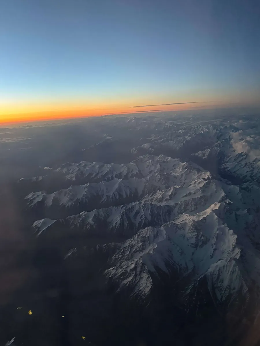 Blick aus dem Flugzeugfenster auf verschneite Berge im letzten Abendlicht